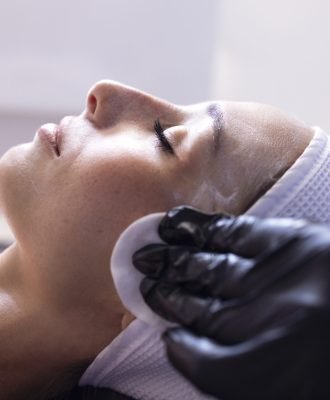 Close up of beautiful young brunette woman during facial cleansing and massage. Cosmetic procedures in a beauty salon or clinic. Lighted candles on background. Skin care and health concept.
